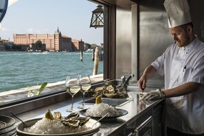 A chef preparing oysters with a view of a river and buildings in the background. - La Calcina Suites (Venice)
