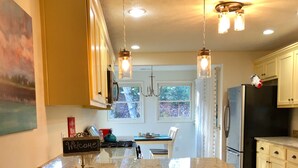 Una cocina con una isla central, taburetes de bar, un refrigerador y un comedor con vista a árboles.