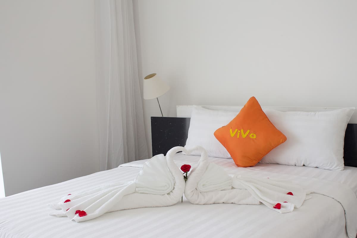 Een net opgemaakt bed met witte lakens, een enkel oranje kussen met 