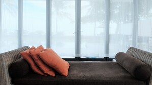 A modern living room with a sofa and two cushions, large windows with sheer curtains, and a view of palm trees outside. - Viva Villa Sanctuary Ho Tram (Ho Chi Minh City)