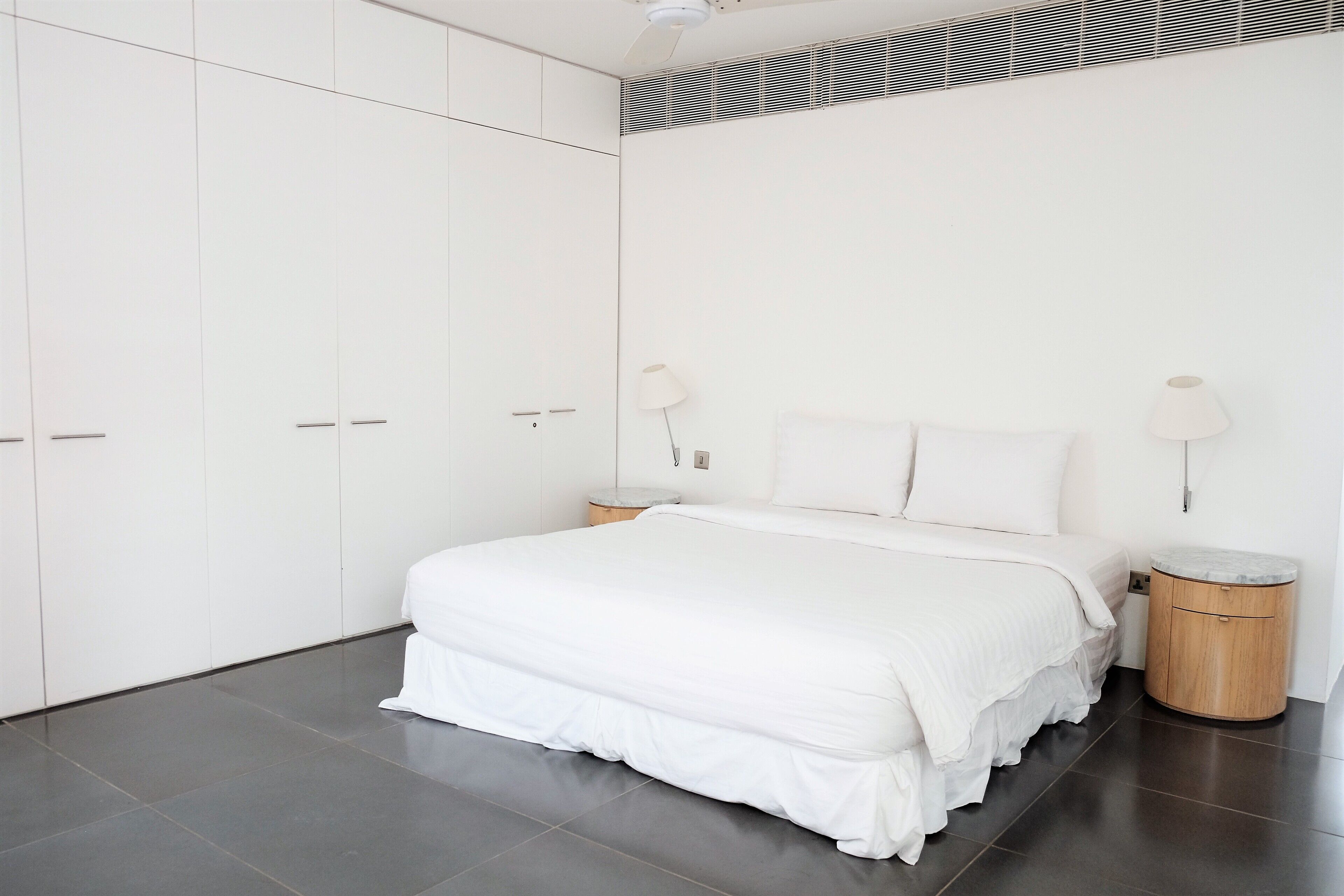 A modern bedroom with a large bed, white bedding, a bedside table, and a wardrobe.