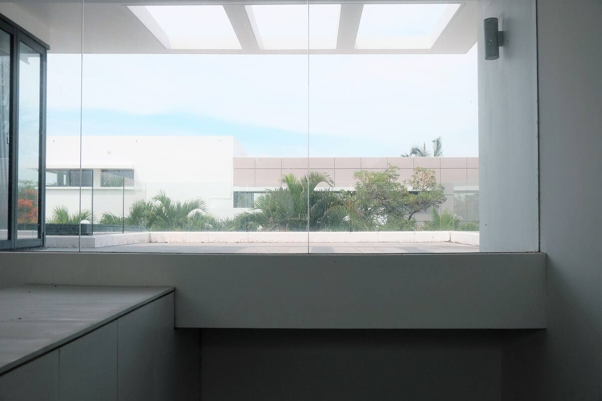 Een moderne kamer met een groot raam, een ingebouwde bank en uitzicht op een gebouw en groen.