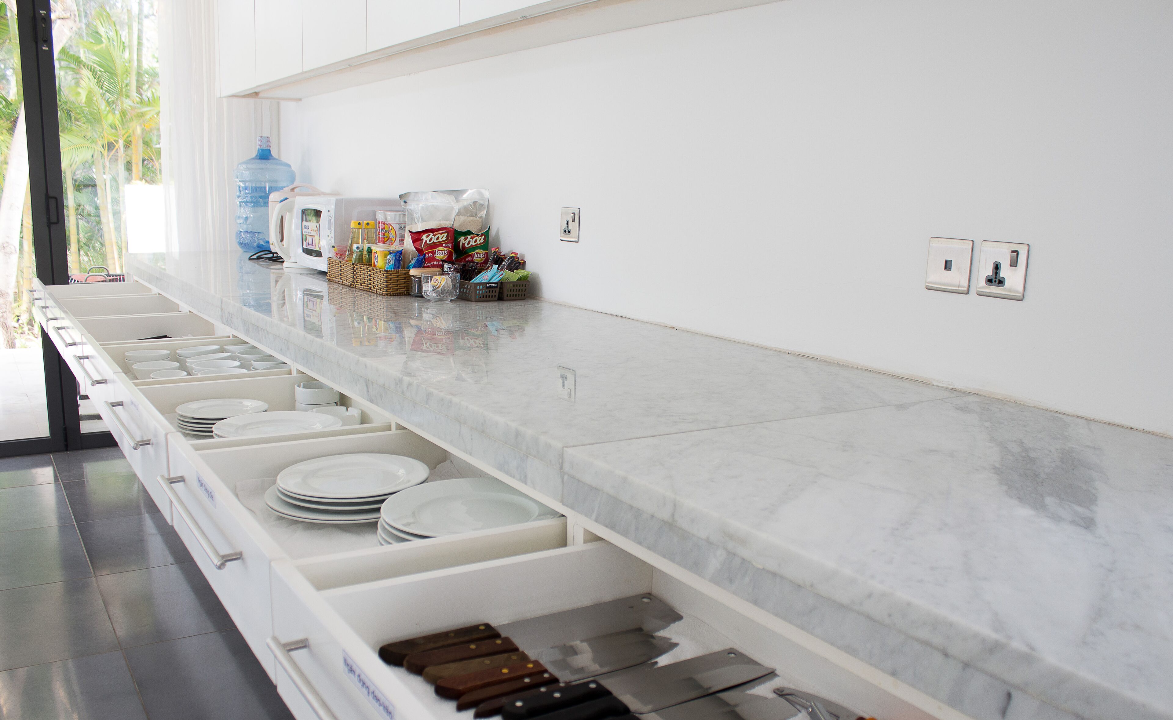 A kitchen with white cabinets, a marble countertop, and various kitchen items like plates and utensils.