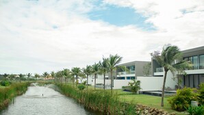 A modern building with a water channel, palm trees, and a clear sky. - Viva Villa Sanctuary Ho Tram (Ho Chi Minh City)