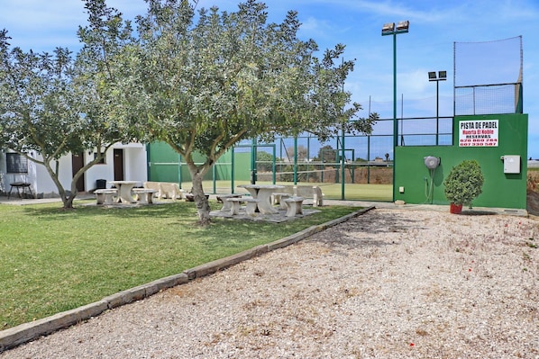 Una puerta verde con un letrero, cancha de tenis y mobiliario exterior.