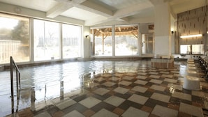 Piscina interior ampla com paredes de vidro transparente, piso xadrez e área de deck de madeira visível pelo vidro.