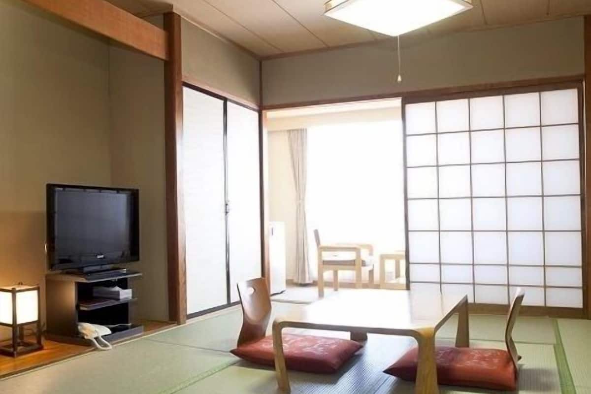 A traditional Japanese room with tatami flooring, a television, and sliding doors.