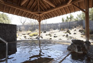 Un espace extérieur abrité avec un jacuzzi, agrémenté d’un mur en pierre et d’une clôture en bois en arrière-plan.