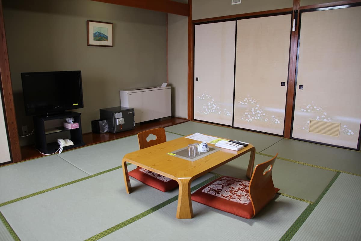 A traditional Japanese room with tatami flooring, a low table with cushions, a television, and sliding doors.
