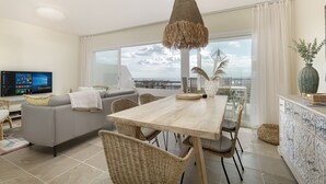 A modern living room with a grey sofa, a wooden dining table, wicker chairs, and a large window offering a city view. - ☀Sun-flooded house / ☀ Panorama sea view & pool (Manilva)