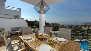A balcony with a wooden table set for dining, a hanging light fixture, and a view of the sea and buildings. - ☀Sun-flooded house / ☀ Panorama sea view & pool (Manilva)