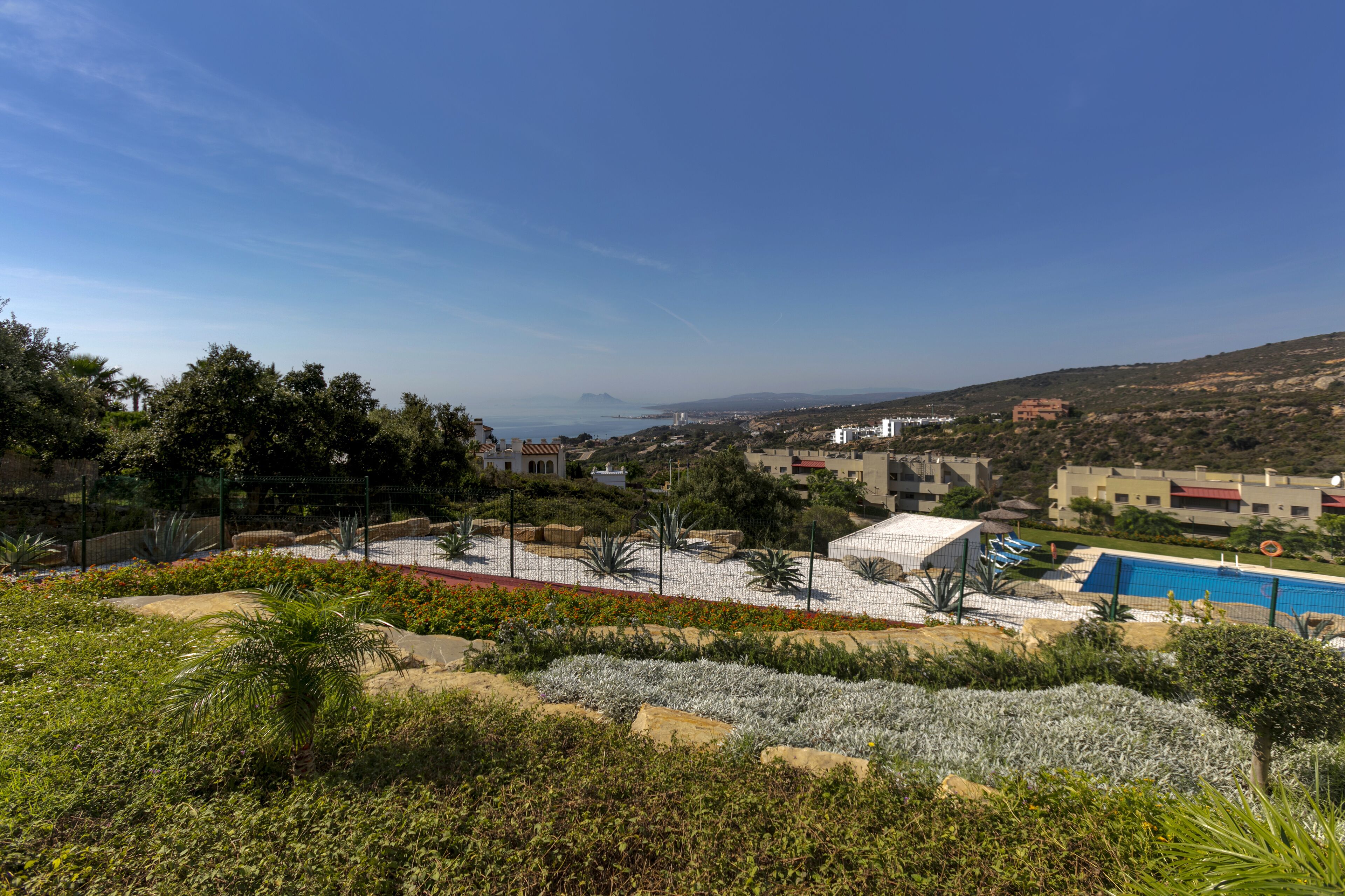 A resort with a pool, landscaped garden, and views of the sea and distant buildings.
