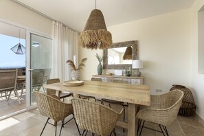 A dining area with a wooden table, wicker chairs, a hanging light fixture, and a large mirror on the wall.
