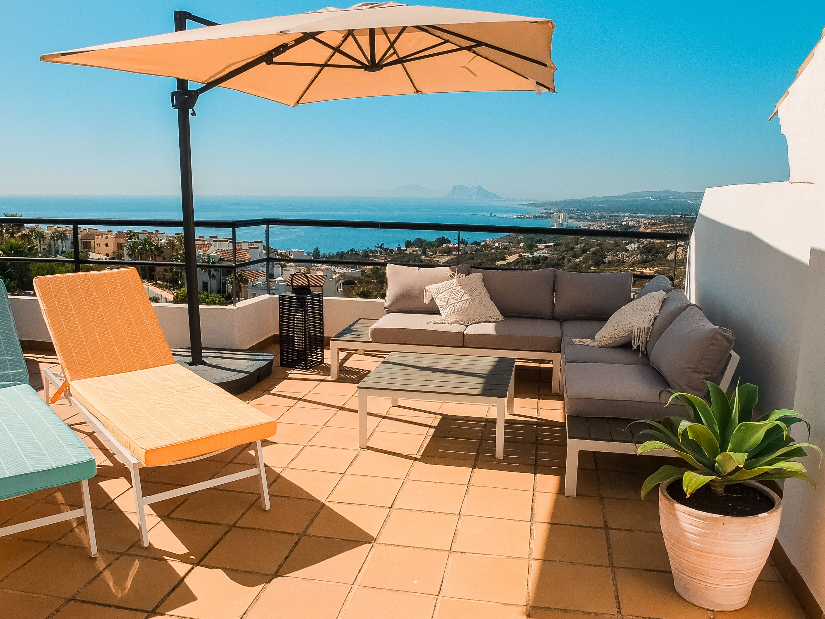 A terrace with a sofa, chairs, and a table, overlooking a coastal view.