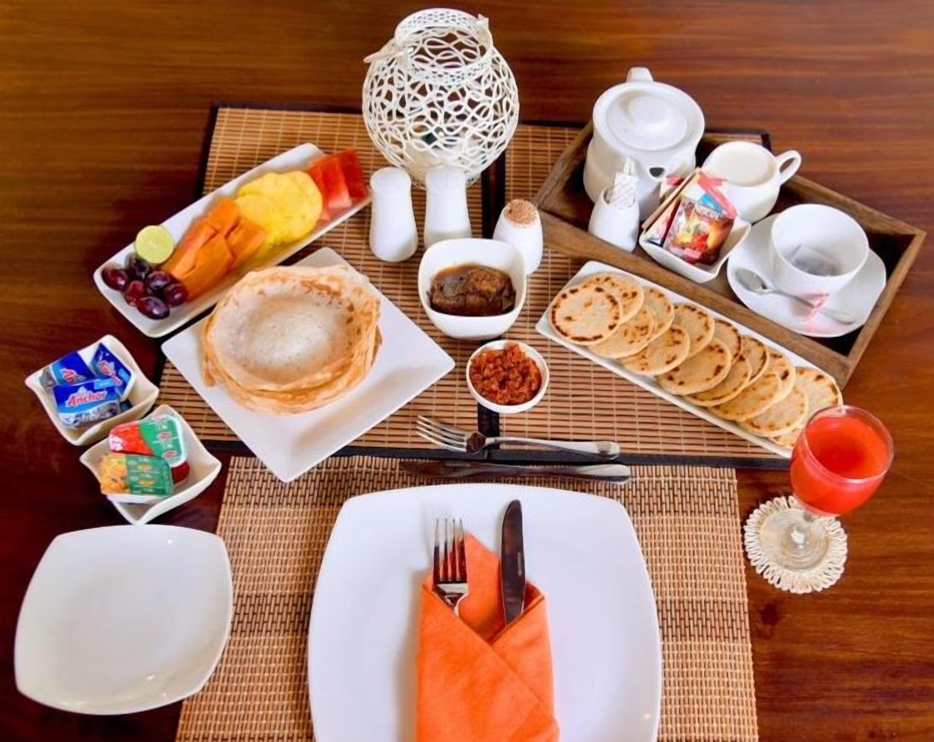 A breakfast setting with various food items, utensils, and a decorative centerpiece on a wooden table.