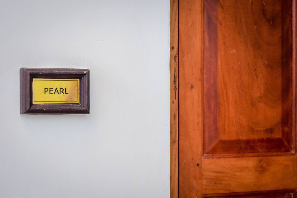 Een houten deur met een plaquette waarop ‘PEARL’ staat, tegen een witte muur.