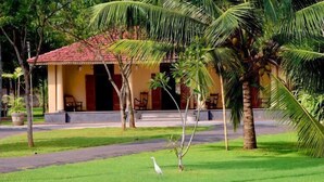 A building with a red-tiled roof, surrounded by palm trees and a grassy area. - Ayurveda Villa 386 (Balapitiya)