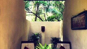 A covered seating area with two wicker chairs, a wooden table with a book and a potted plant, and a ceiling fan. - Ayurveda Villa 386 (Balapitiya)