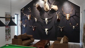 Una habitación con mesa de billar, sofás y una pared decorada con cráneos de animales.