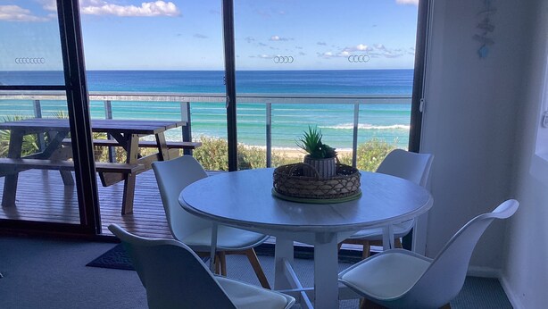A round table with white chairs and a potted plant in the center, overlooking a beach with turquoise waters and a clear sky. - Bluecrest 2 at Blueys Beach (Blueys Beach)