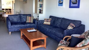 A living room with two blue sofas, a wooden coffee table, and a wicker chair. There is a bookshelf with books and framed pictures on the wall. - Bluecrest 2 at Blueys Beach (Blueys Beach)