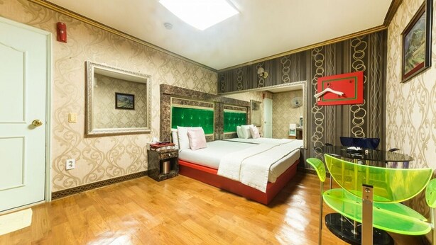 Un dormitorio con cama, mesita de noche, espejo y una silla verde.