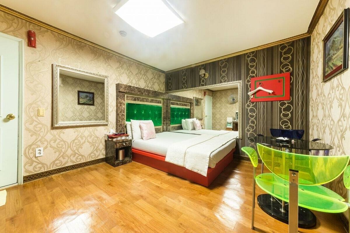 Ein Schlafzimmer mit Bett, Nachttisch, Spiegel und einem grünen Sessel.