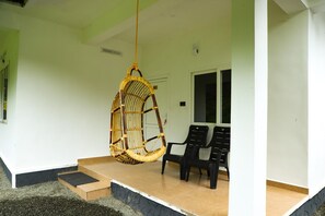 Une pièce avec un fauteuil suspendu, deux chaises noires, une petite plateforme en bois et une fenêtre.