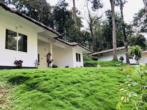 Un bâtiment blanc coiffé d’un toit de chaume, entouré d’une végétation luxuriante et d’arbres.