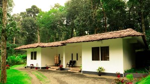 A single-story building with a tiled roof, a porch with chairs, and potted plants.