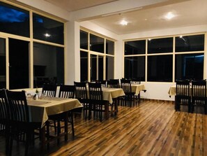 Un espace repas comprenant plusieurs tables et chaises, de grandes fenêtres et un plancher en bois.