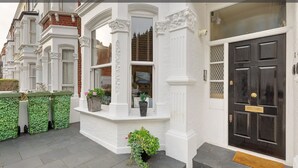 A Victorian-style townhouse with ornate white trim, a black front door, and green planters.