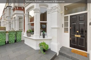 Traditional townhouse with a classic exterior, featuring a bay window and a small balcony with potted plants.
