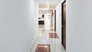A modern hotel corridor with a clean, tiled floor and a wooden door on the right. - Capital O 63727 Mythri Hotel (Hyderabad)