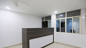 Un espace d’accueil avec un comptoir de réception sombre, des murs blancs et un sol carrelé.