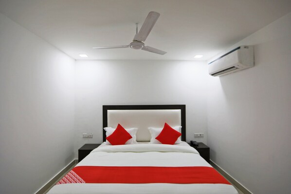Une chambre d’hôtel équipée d’un lit, d’un ventilateur de plafond, d’un climatiseur et d’une table de chevet avec une lampe.