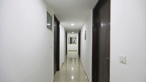 Un couloir étroit et bien éclairé, aux murs blancs et au sol brillant, qui mène à une porte au fond.