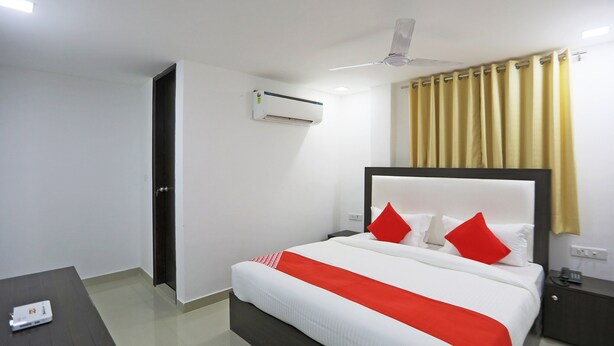 Une chambre d’hôtel comprenant un lit, une table de chevet, une commode, un appareil de climatisation, un ventilateur de plafond et une fenêtre avec des rideaux.