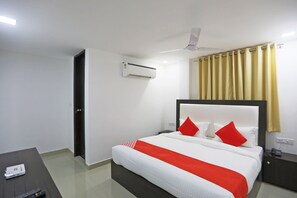 Une chambre d’hôtel comprenant un lit, une table de chevet, une commode, un appareil de climatisation, un ventilateur de plafond et une fenêtre avec des rideaux.