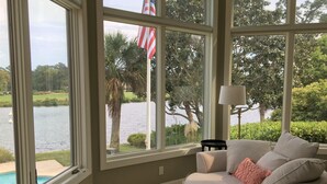 Una habitación con ventanas amplias que dan a un lago, una bandera y una lámpara.