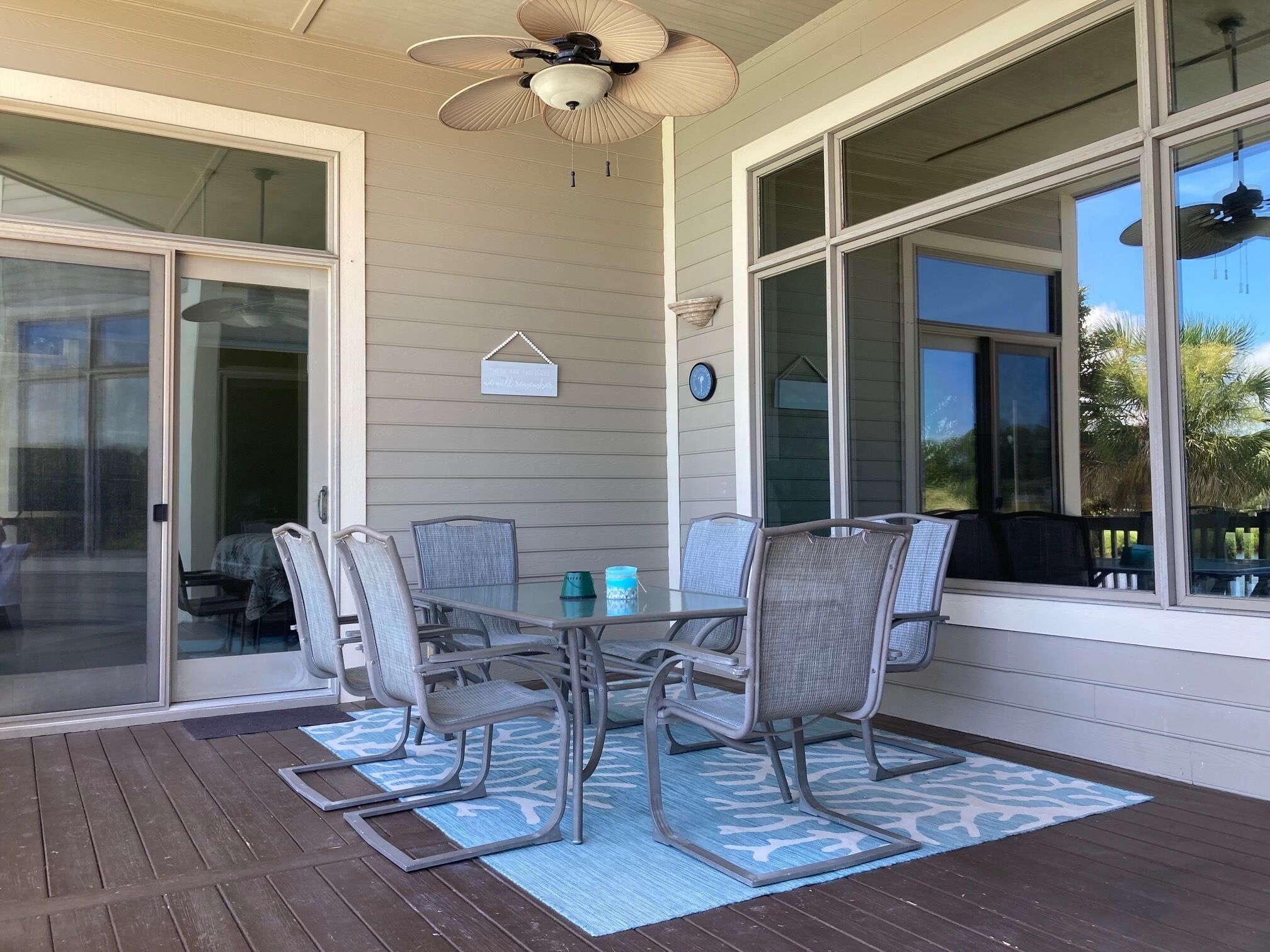 Eine überdachte Terrasse mit Tisch und Stühlen, großen Fenstern und einem Deckenventilator.