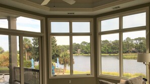 Una habitación con amplias ventanas que dan a un lago, una terraza y una silla con cojines.
