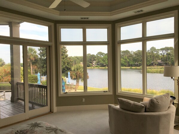 A room with large windows overlooking a lake, a deck, and a chair with cushions.