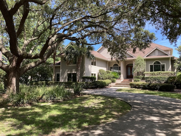 A two-story house with a front porch, a driveway, and a large tree in the foreground.