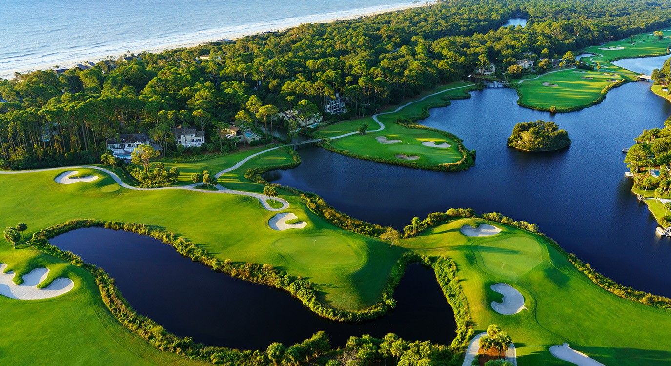 Un parcours de golf avec des obstacles d’eau, entouré d’une forêt dense et bordé par un plan d’eau.