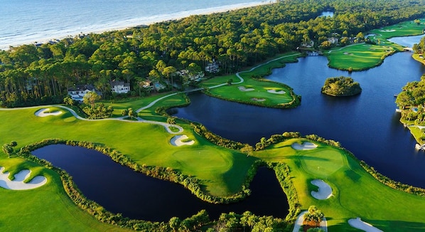 A golf course with water hazards, surrounded by dense trees and a body of water.