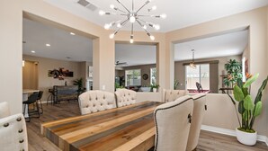 A spacious dining area with a large wooden table, upholstered chairs, and a modern chandelier.