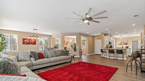 A spacious living room with a large red rug, a grey sofa, and a ceiling fan.