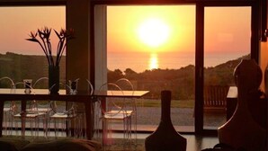Et værelse med et spisebord og stole, en vase samt udsigt til solnedgang over vand.