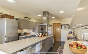 Una cocina moderna con un refrigerador de acero inoxidable, horno empotrado y una isla grande con un cuenco de frutas.